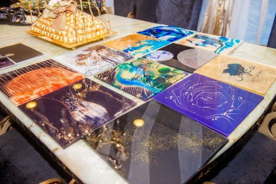 The picture shows a close-up of an orange rose with its five petals displayed. In the center of the flower is a yellow stamen. There are green leaves surrounding the rose, and some are gently touching it.