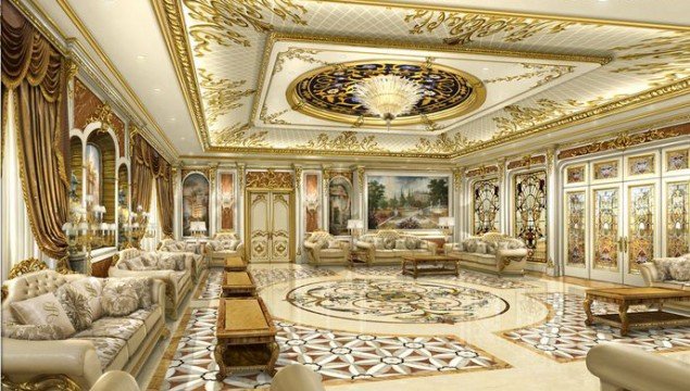 Luxuriously appointed open plan living area featuring a plush sofa and matching armchairs, ornate chandelier, and intricate ornamental patterns on walls and carpets.