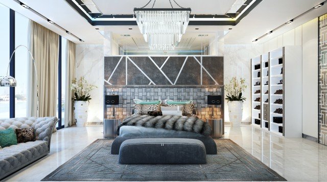 This picture shows a woman wearing a light blue tank top and standing in a sunlit room. She is holding her arm across her chest with her hand resting on her opposite shoulder. The room has white walls and hardwood floors, and there is a white chair next to her. The sunlight is creating a warm glow in the room and the woman looks relaxed and content.