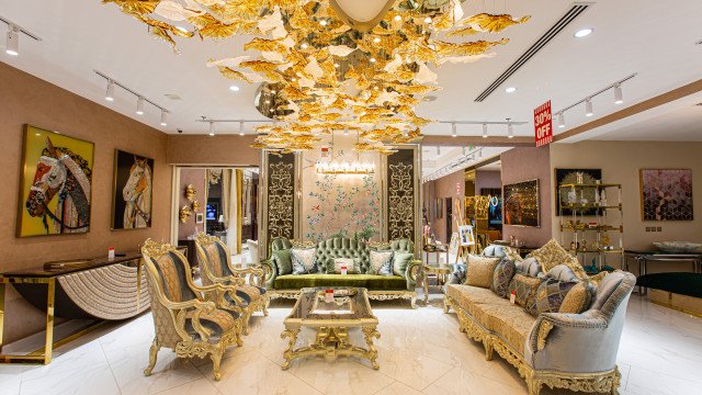 The picture appears to show a luxurious living room with a dark wood floor and a large red velvet sofa facing a fireplace. On either side of the sofa are two end tables with lamps and there is also an area rug below the sofa. The walls are a cream color and decorated with several portraits and decorative items.