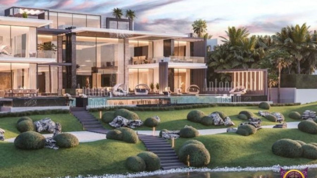 This picture shows a contemporary style living room decorated with plush white furniture, modern art, and warm wood accents. The walls are painted in a light gray with white trims, while the ceiling features recessed lighting. The center of the room is occupied by a white, round rug featuring spiral designs, and the space is populated with various pieces of modern, abstract art. In the corner of the room, two small, green plants lay perched atop a golden table, adding a touch of nature to the otherwise modern home.