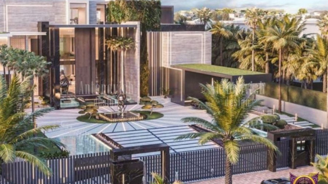 This picture shows a modern, luxury living room designed by Antonovich Design. It features a cream-colored sofa with gold accents and a tufted back, along with two armchairs in a contrasting navy blue fabric. A black-painted fireplace with a large mirror above it serves as a focal point of the space. The walls are painted a light gray hue, and natural light shines in through an open window framed with sheer curtains. A low, glass-top coffee table sits in the center of the room, accompanied by a large abstract painting on the wall behind it.