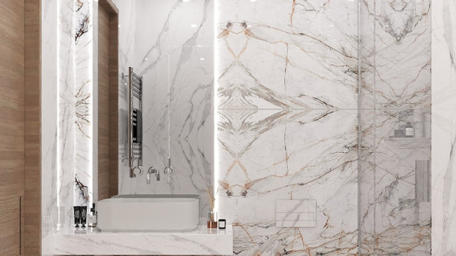 The picture depicts a modern luxury living room with dark grey velvet couches and armchairs, an abstract patterned ottoman in the center of the room, and teal and white patterned curtains along the walls. There is an ornate grey mirror on one wall, and a large abstract painting hangs on the opposite wall. The ceiling is painted white and features recessed lighting.