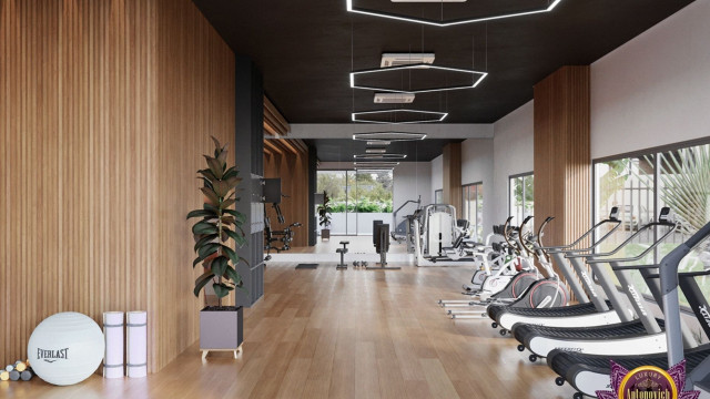 This picture features a modern interior design featuring a white ceiling with recessed lighting. The walls are painted in a light color with a shimmering metallic strip running along the bottom of the wall. The floor is dark and made of hardwood, while the furniture is upholstered in shades of cream and brown. The centerpiece of the room is a large leather sofa with a thin chrome frame, flanked by two modern chairs, and a mid-century style coffee table in the center.
