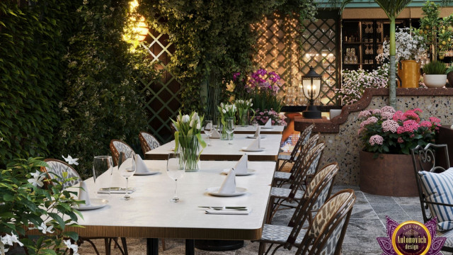 This picture shows a luxurious modern living room, featuring a white and neutrally toned color palette with a hint of grey. The living room is comprised of a white tufted sofa with a matching ottoman, a glass coffee table, and two plush armchairs. The walls are decorated with artwork to give the room a cozy and inviting atmosphere. There is also a large built-in bookshelf spanning one wall, filled with books and decorative accents.