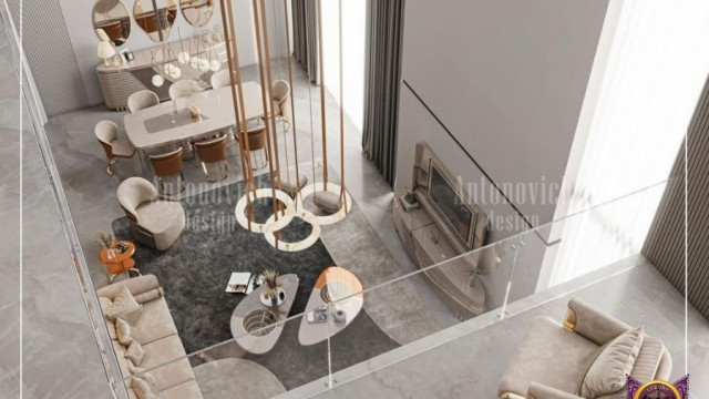 This picture shows a modern, stylish living room. The room features a large, white sectional sofa and an ottoman in the center of the room. The walls are adorned with abstract artwork, and there is a contemporary black marble fireplace mantel with a wall-mounted television above it. Two oversized windows allow natural light to fill the room, and the wood flooring adds warmth to the design. Lastly, there is a blue rug to tie all the elements together.