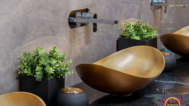 The picture shows a luxurious living room with a white carpet, white walls, and a large grey sectional couch. On the wall, there is a large gold-framed painting. Behind the sofa, there is a glass wall overlooking a large body of water. There are two armchairs in the room, as well as a round coffee table between the seats. The room also features a modern, stylish chandelier.