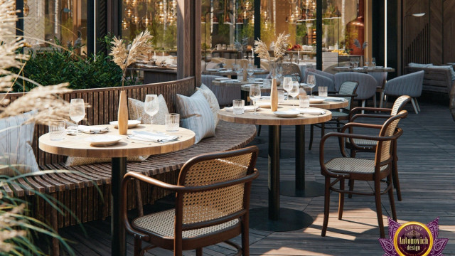 This picture shows a luxurious and contemporary living room designed by Antonovich Design. The room features a beige and charcoal color palette with pops of gold, creating a glamorous and inviting atmosphere. There is an impressive and large light fixture suspended from the high ceiling, and a stunning stone wall that adds warmth and texture to the aesthetic. The furniture is soft and plush and includes sofas, chairs, and tables, all in neutral tones.