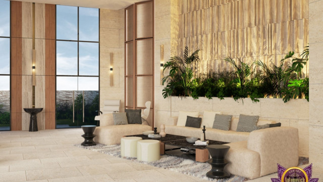 This picture is showing a contemporary living room with vaulted ceilings, featuring a curved sofa and two armchairs in a neutral color scheme. The walls of the room are painted white and adorned with modern artwork. A round dark wooden coffee table sits in the center of the space, and a blue and white patterned rug grounds the area. The floor-to-ceiling windows allow for plenty of natural light and provide a view of the outdoors.