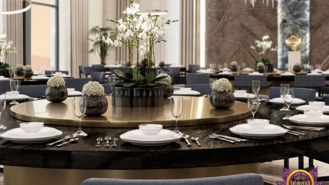 This picture shows a modern luxury living room designed by Antonovich Design. It features a large gray velvet sofa, flanked by two white armchairs. There are two matching side tables with a black marble top, and a central glass table, all surrounded by a circular rug. The walls are decorated in a light gray and white wallpaper pattern, and there is an abstract art piece on the wall. The room is finished with contemporary lighting and black and gold accents.