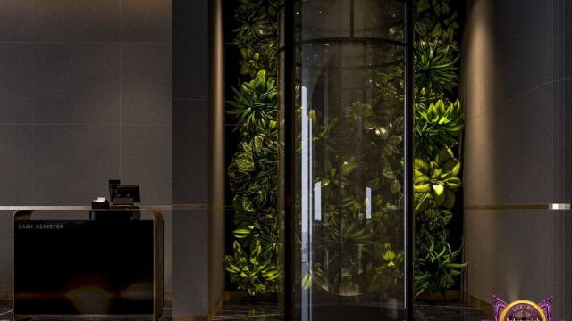 This picture shows an elegant modern living room with a large sofa and two armchairs facing a wooden coffee table. The walls are painted with a light grey color that contrasts with the black furniture, while plenty of natural light is entering the room through the large windows. There are several accent pieces including bright blue cushions, a classic white clock, and a modern pendant light.