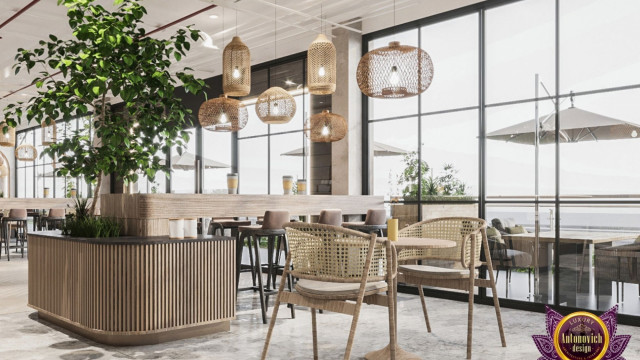 This picture shows a modern living room with an open-concept design. The room features a large white sectional sofa, two armchairs, and a large ottoman that serves as both a footrest and coffee table. A sleek gas fireplace is centered in the wall, and a glass wall separates the living room from an outdoor patio. The walls are painted a light gray color, while the furniture and accents provide pops of color, making the space warm and inviting.