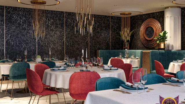 This picture shows a modern contemporary-style living room with white walls, a large grey sectional couch, a glass coffee table and two small side tables, and a gray and white patterned rug. The room is accented with colorful throw pillows, a metal and glass chandelier, and a wall mirror.