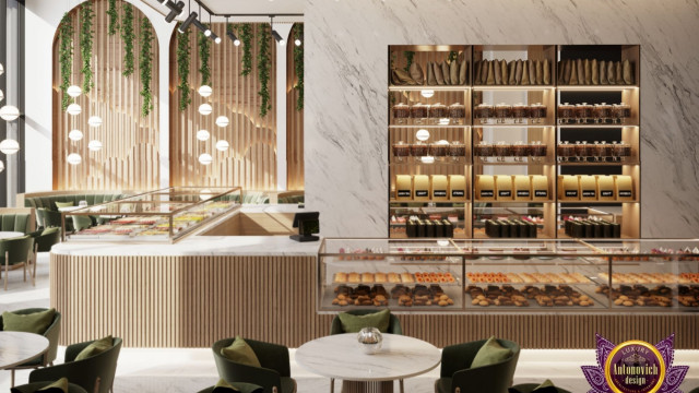 This image shows a luxurious, modern living room with a white marble floor, a black velvet sectional couch, and a blue tufted armchair with dark wood legs. The walls are painted a light gray color and there is a large flat-screen television mounted on the wall. On the coffee table, there is a black vase filled with white roses, and two decorative glass and brass lamps. The room also has a white fireplace with a gold-accented mantle.