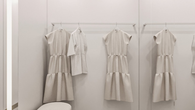 This picture shows a modern living room with a gray and white color palette. The room features a large sectional couch, set in front of a striking wall mural featuring abstract shapes and patterns. The walls are lined with white built-in shelving and lighting fixtures, and the floors feature light wood-look tile. An accent chair and an oversized ottoman are situated off to the side, and the room is decorated with colorful framed artwork and greenery.