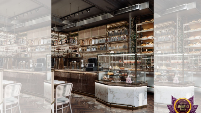 This picture shows a modern, luxury kitchen designed by Antonovich Design. The room features glossy white cabinets and a large island with black countertops. There is a built-in oven, a stainless steel refrigerator, and a range with a hood. The walls are decorated with modern artwork and there are recessed lights in the ceiling.
