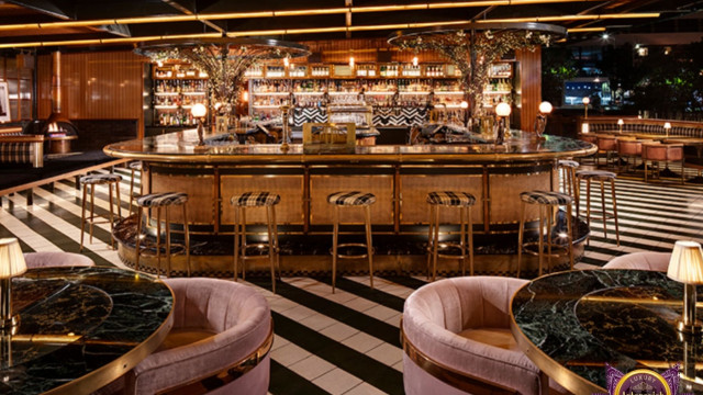 A traditional European-style living room featuring a statement fireplace mantelpiece, a wall-mounted portrait, upholstered furniture, and patterned drapery.