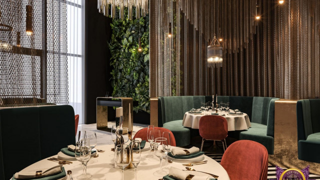 This picture shows a modern, luxurious kitchen designed by Antonovich Design. The kitchen is white with gray accents and has a large center island with seating space. The countertops are made of marble, and the cabinetry is sleek with stainless steel handles. There are two built-in ovens, a gas range top, a built-in microwave, and a double door refrigerator. There are also several windows that allow natural light to flood the room.