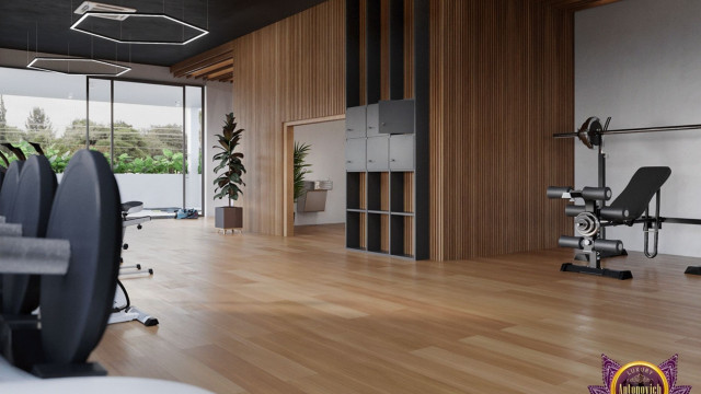 This picture appears to be a bedroom in a luxury home. The walls are painted a light grey color, and the floor is covered in a plush light-colored carpet. There is a white bed with several pillows and a large, dark grey headboard at the center of the room. On either side of the bed is a small nightstand with a light fixture. On the right side of the bed, there is a small wooden desk and chair, as well as a tall lamp. Along the wall opposite the bed, there is a tall black cabinet with several drawers and shelves.