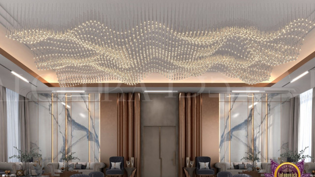 The picture shows a luxurious modern living room. The walls are painted white, with a grey sofa situated in the center of the room. There is a round coffee table in front of the sofa and two armchairs on either side. The armchairs are upholstered with a patterned fabric and have a unique curved shape. On either side of the living room are tall windows that bring in plenty of natural sunlight. A black marble fireplace is set into the wall and a beautiful framed artwork hangs above it.