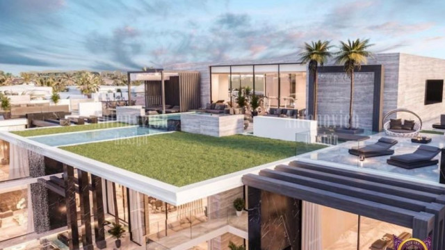 The picture shows a luxurious living room with classic white and gold decor. The walls are painted in an ivory color and the trim is gold. The large chandelier in the middle of the room provides a glamorous touch to the space. A grand piano is placed near the window, which overlooks lush landscaping outside. Two tufted armchairs and a white sofa provide comfortable seating in the center of the room. The beige rug on the floor ties the room together and adds a warm touch to the overall design.