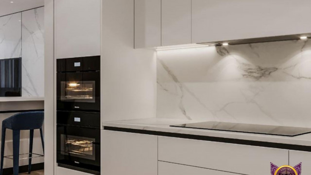 This picture shows a modern, minimalist kitchen featuring a built-in stainless steel oven, a sink with a contemporary black faucet, and a white quartz countertop with a gray marble backsplash. There is also a gray tile floor and a large window with sheer curtains allowing natural light to fill the space.