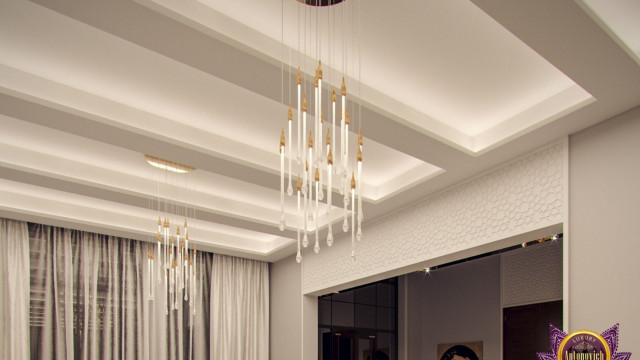 The picture shows an interior design with a large white sofa in the center of the room. The walls are painted gray and there is a curved wall separating the living area from the dining area. The living area has two armchairs and several potted plants, while the dining area has a round dining table with six chairs placed around it. The floor is covered in a parquet pattern, while the ceiling has several exposed wooden beams.