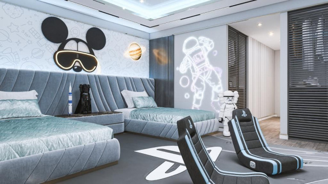 This picture shows an outdoor living space featuring a white lounge area with three chairs and a sofa set on a wooden deck. The furniture is covered in colorful pillows, and a white rug is visible on the floor. There is a trellis structure in the background, with a variety of plants, including ferns and ivy, planted along the walls. A brick pathway leads away from the seating area.