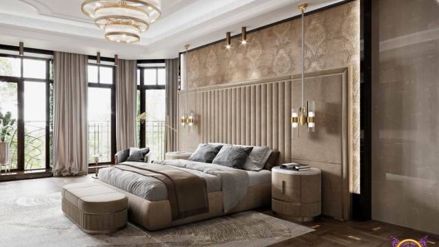 The picture shows a modern bedroom with an upscale design. The room features a light grey wall and a white ceiling. There is a large window with a sheer white curtain that lets in a lot of natural light. The bed has a white upholstered headboard and footboard, and white bedding. The nightstands are also white with brass accents. On the walls, there are patterned wallpapers in neutral colors that match the rest of the decor.