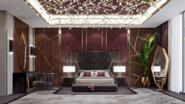 This picture shows an ornate picture frame with an intricate design. The frame is painted a dark shade of red and decorated with gold accents. Behind the frame is an upholstered seating area with a white-on-black patterned throw pillow. In the background there is a tall candle holder adorned with several votives.