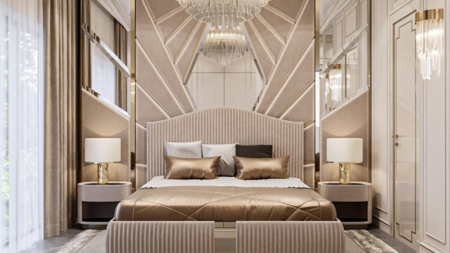 This picture is showing an above view of a modern and luxurious bedroom. The room features a large king-size bed dressed in white linens, a plush cream-colored carpet, an ornate curved gold-framed mirror, two velvet chairs arranged with a small table between them, and several tall white pillars that support a draped canopy over the bed.