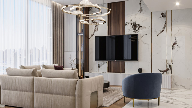 This picture shows an ultra modern living room with dark furniture and accents paired with a white and grey palette. The room features a long, tufted sofa and two matching armchairs. There is an area rug in the center of the room and various accent pieces such as a large mirror, two glass vases, and a modern chandelier. The walls are painted a light grey color with a chrome trim along the edges, creating a sleek look.