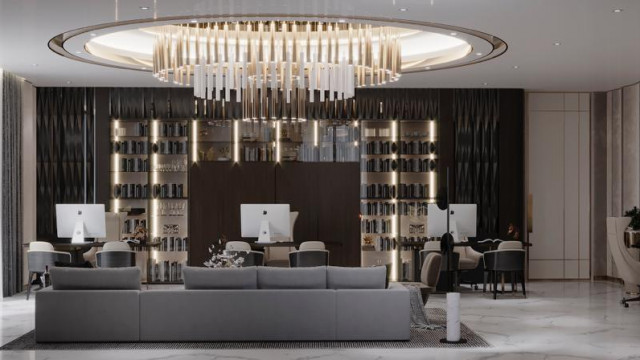 This is a picture of an interior design that features a modern living room with two armchairs upholstered in grey fabric, set on opposite ends of a cream and gold rug. The walls are painted in a light shade of grey, and the space is filled with natural light coming in through the large windows. A black accent wall is visible at the back of the room, highlighting the minimalist design.