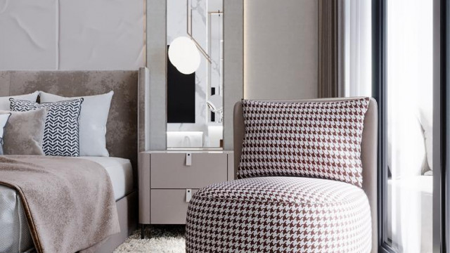 The picture shows a luxury living room with modern decor. The furniture is dark wooden and includes a sofa, two chairs, an ottoman, and a coffee table. The walls are a light beige color and there is abstract art hanging on the wall. The lighting fixtures are suspended from the ceiling and have a sleek, contemporary design.