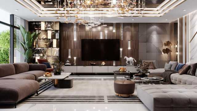 The picture shows a modern living room design featuring an oversized light gray velvet sectional sofa, a round glass coffee table, and white accent chairs. The walls are painted a soft shade of beige, and two large windows with sheer white curtains allow natural light to flood the area. A large abstract painting hangs on one wall, while a geometric rug in shades of gray, white, and navy ties the entire room together.