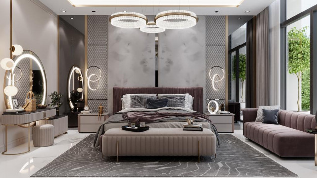 This picture is of a luxury living room designed by Antonovich Design. It features a large, traditional style sofa upholstered in a rich, classic pattern and a matching ottoman. The walls are decorated with an extravagant gold mirror, ornate framed artwork, and black and white accents. A elegant white ceramic table lamp and a modern glass chandelier add accents of sparkle and sophistication to complete the look.