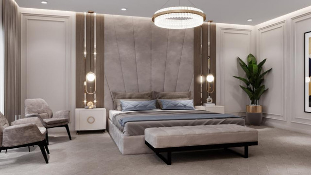 The picture shows an elegant living room with a modern design. It features a large white leather couch with cream colored pillows, a glass coffee table, and a plush white rug. The walls are painted in a warm gray color and there is recessed lighting throughout. On the far wall, there is a beautiful wall art piece featuring a gray, abstract painting surrounded by black metal framing.