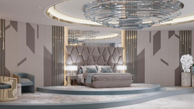 In this picture, we can see a large, contemporary living room with a brown leather sofa, white armchairs, and a matching ottoman around a large glass-top coffee table. There are also several abstract art pieces on the walls and a white fireplace in the corner. The floor is covered in a large area rug and there is an array of potted plants to add a touch of greenery. Overall, the room has a modern yet comfortable feel.