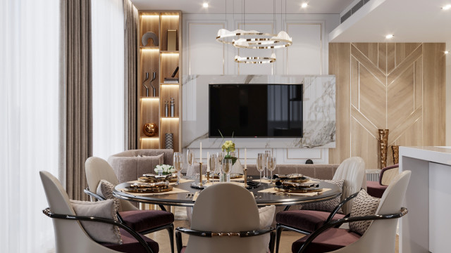 The picture shows an expansive, luxurious living room with a beige, grey, and gold color palette. The room features a large, white leather sofa and two matching armchairs, which are placed around a round, gold-colored coffee table. There is a white fireplace with a gold inlay above it, and two light-colored area rugs are placed on the floor, along with a dark wooden sideboard. There is a tall, arched window that lets in plenty of natural light, and the walls are decorated with various art pieces.