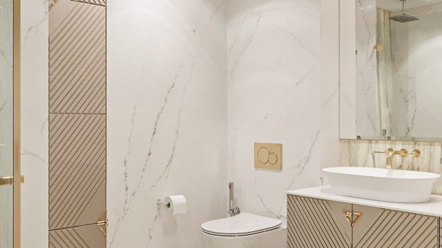 This picture shows a luxurious bathroom with beige and gold marble flooring, white walls, intricate gold-trimmed mirrors, and a gold chandelier. There is a porcelain corner tub in the center of the room, surrounded by wooden cabinets and several plants that bring life and color to the space. A white shower curtain hangs from the wall next to the corner tub, and a plush beige rug lies on the floor.