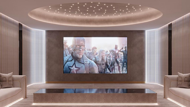 This picture shows a luxury living room with a white and gold color palette. The walls are painted white, and the furniture has upholstery in gorgeous white and gold fabrics. In the center of the room is a round glass coffee table with a marble insert, surrounded by four comfortable-looking sofas. There are also several side tables around the space, as well as a grand chandelier hanging from the ceiling.