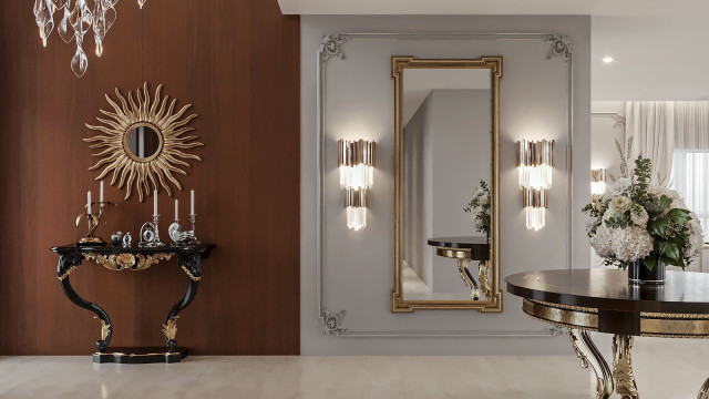 This image shows a modern luxury living room with a stunning view of the cityscape. The room has a white marble floor, modern furniture, and a large grey velvet couch. On the left side of the room, there is a fireplace and a glass coffee table with a unique patterned rug beneath it. A large flat-screen television hangs above the fireplace, and a pair of abstract paintings adorn the walls. There is also a modern bar in the corner stocked with colorless bottles.