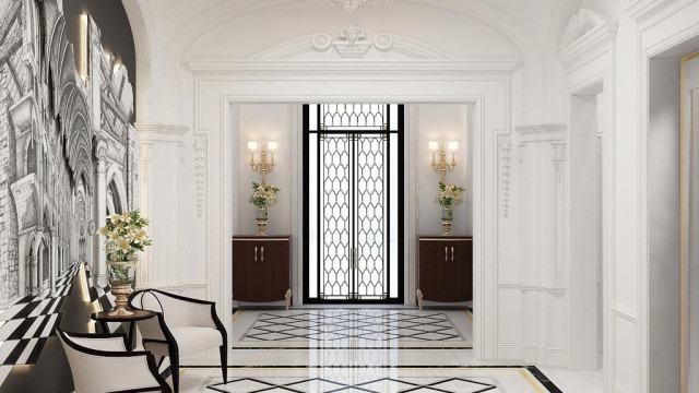 The picture shows a luxurious, modern bedroom with an elegant white and beige color scheme. The focal point of the room is the large four-poster bed which stands on an ornately patterned rug in shades of beige and brown. The walls are decorated with an eye-catching mural depicting an idyllic beach scene. Other features of the room include a built-in set of cabinets and drawers, a chaise lounge chair, and an upholstered armchair. A crystal chandelier hangs from the ceiling, providing a touch of glamour to the space