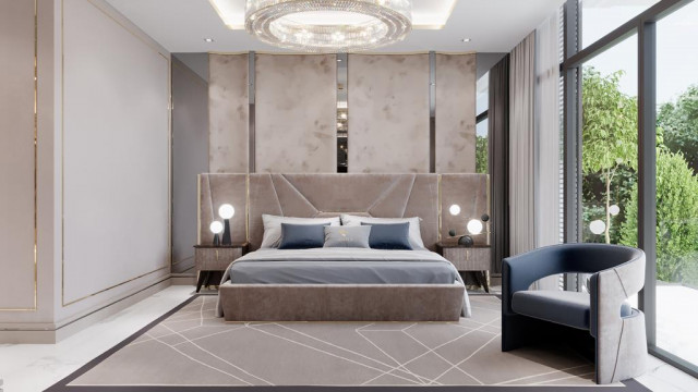 This picture is showing a modern bedroom with hardwood floors and white walls. The bed is covered with a blue and white duvet, and there is a white nightstand next to it with a lamp on top. The headboard of the bed has a unique geometric pattern that adds texture and interest to the room. There are also two chairs in the corner, one colored in light blue and the other in dark grey. Overall, this simplistic yet elegant design makes for a relaxing and inviting space.