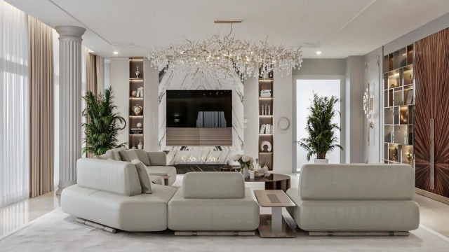 This picture shows a modern and luxurious interior design. The space features a sleek white floor, white walls and ceiling, and dark blue furniture. There is a contemporary fireplace against one wall, while the other wall has a wall-mounted flat screen television. In the center of the room is a white lacquer dining table, surrounded by six black chairs with gold accents. On the table are two decorative items - a vase filled with white flowers and a wooden bowl with golden balls.