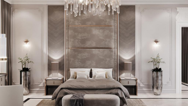 This picture is a rendering of a luxurious modern living room. It features a white and gray color palette throughout, with a light gray velvet sectional sofa and a large round ottoman in the center of the room. On either side of the ottoman, there are two tall armchairs upholstered in gray fabric. Two white coffee tables are situated in front of the sectional sofa, and two mid-century modern style end tables are layered with lamps and decorative accessories. The room is finished with a plush white shag rug, sheer white curtains covering the windows, and