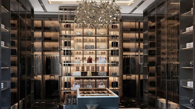 This image shows a living room featuring a modern and luxurious design. The room has a stylish gray color palette, featuring a large sectional sofa and accent chairs in shades of gray, a round black coffee table, and a rectangular rug with a subtle geometric pattern. On the walls, there are several pieces of abstract art in shades of blue and gray. The room is illuminated by multiple recessed lights, and a large crystal chandelier hangs from the ceiling, adding a touch of glamour to the space.
