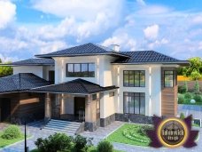 This picture shows two people, a young man and a woman, standing in front of a house. They are both smiling and the woman has her arm around the man's shoulder. The house is a cream-colored two-story with a balcony and several windows. There are trees and shrubs surrounding the house and the sky is bright blue.